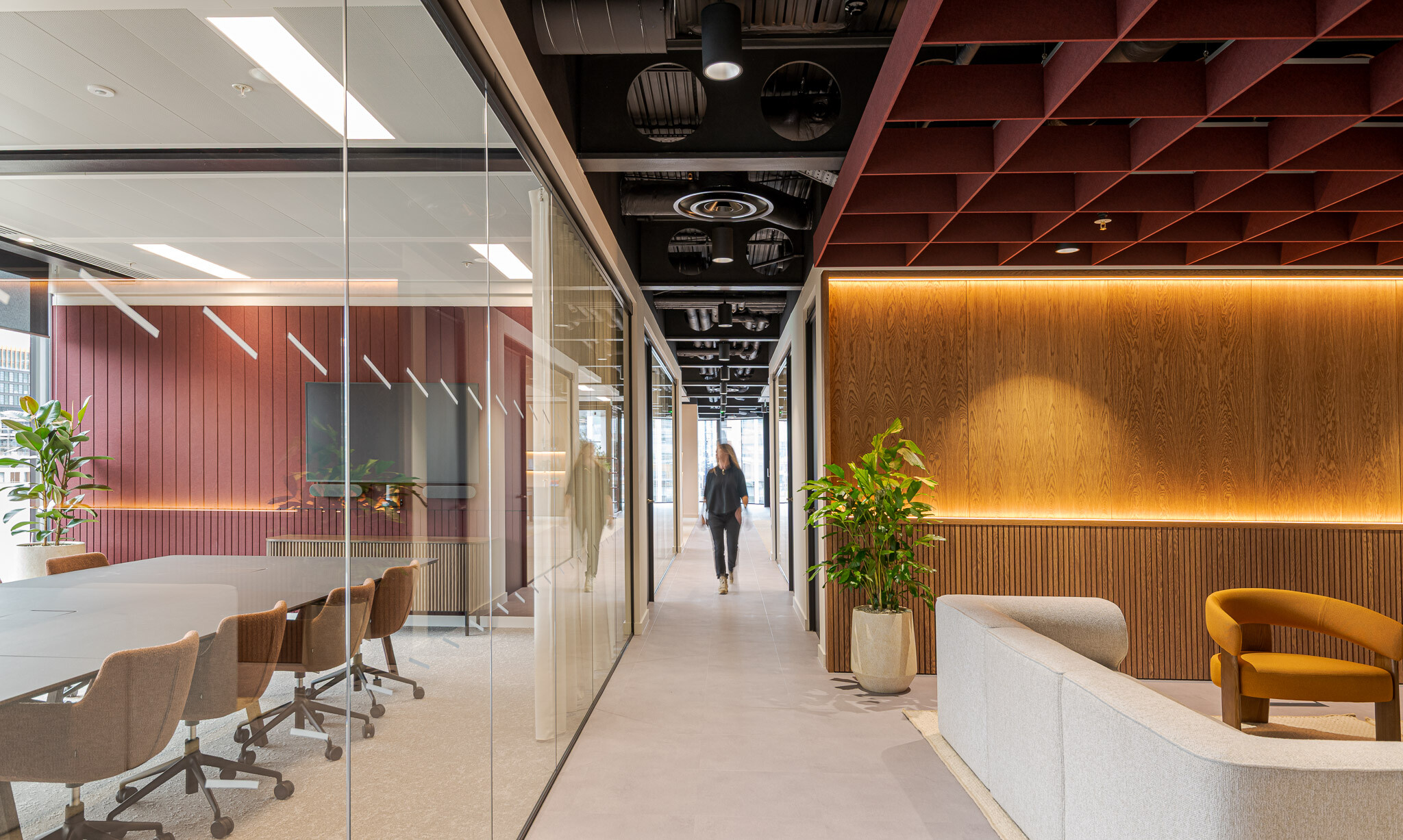 Corridor view of Arbor’s Tenant-Ready™ workspace furnished by Platfform, with a meeting room of mid-tone brown chairs, a curved lounge setup and warm wood wall panelling.