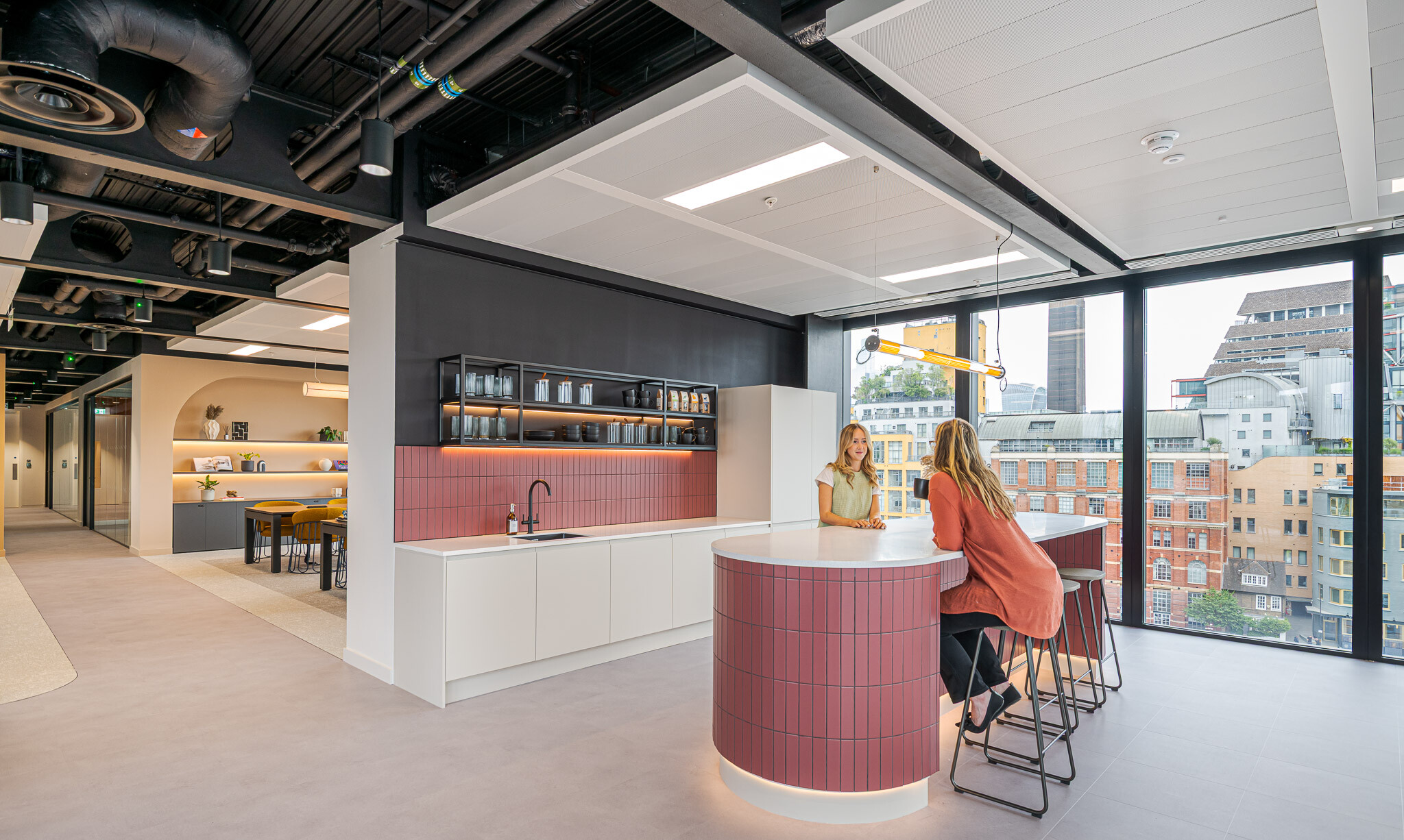 Teapoint area at Arbor’s Tenant-Ready™ workspace furnished by Platfform, with a curved burgundy island, monochrome cabinetry and high stools facing large city-view windows.