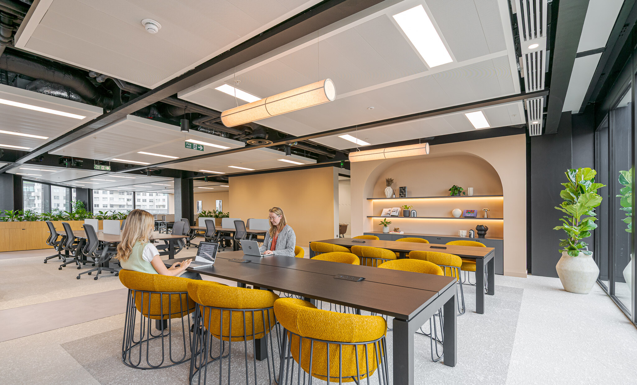 Breakout and hotdesk zone in Arbor’s Tenant-Ready™ workspace, furnished by Platfform, with mustard upholstered chairs, black tables, and built-in shelving under an arched wall.