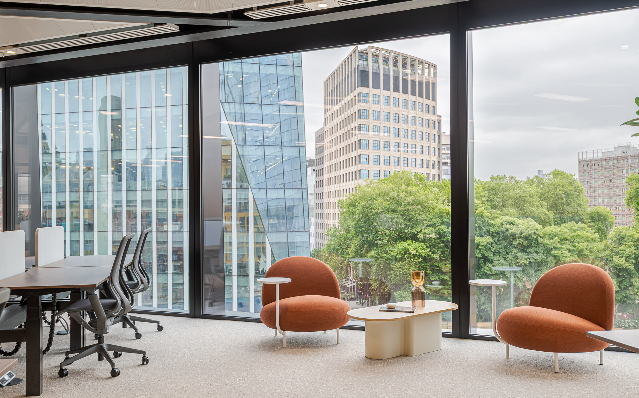 Soft seating area in Arbor’s Tenant-Ready™ workspace, furnished by Platfform, with curved orange chairs and coffee tables overlooking leafy views and modern glass towers.
