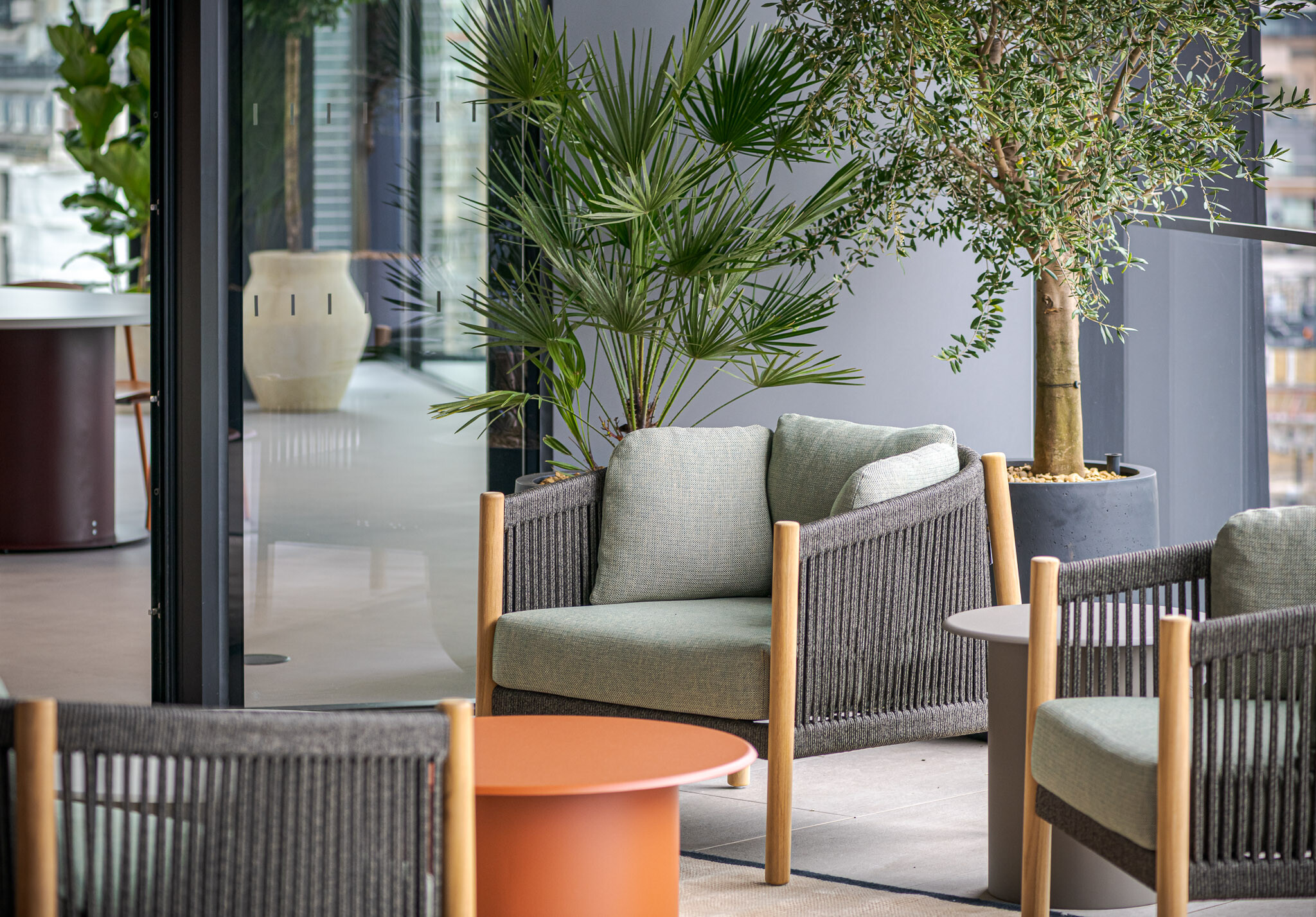 Close-up of terrace seating at Arbor’s Tenant-Ready™ workspace, furnished by Platfform, with rope-framed armchairs, sage cushions, terracotta table and lush potted greenery.