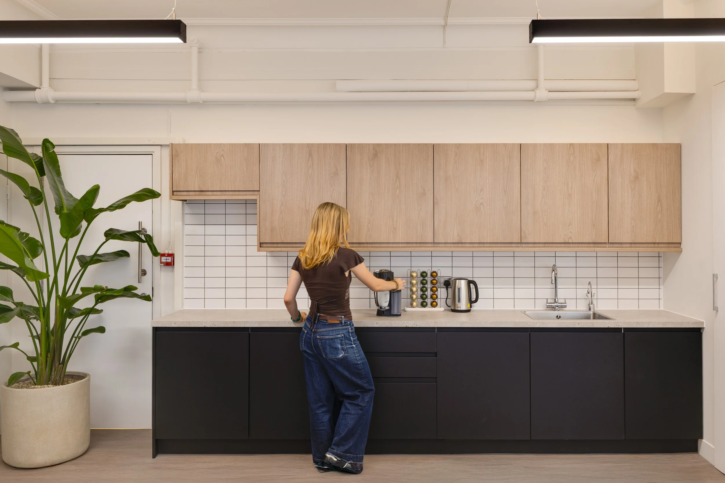 An employee uses the teapoint at InPost’s London office, where Platfform furnished the space with warm oak cabinetry and sleek black units. A simple, functional design makes everyday moments feel part of the office’s rhythm.