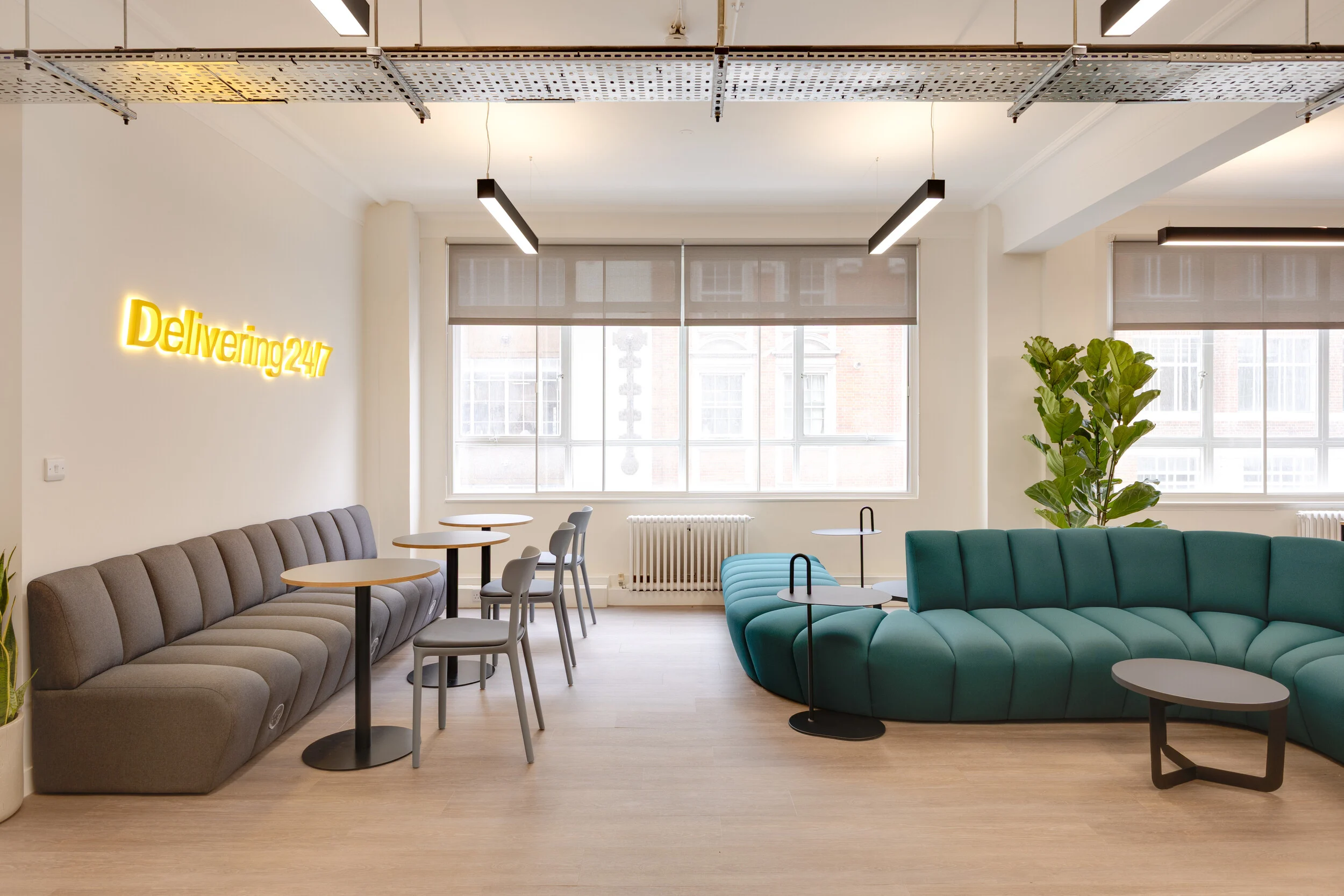 InPost’s breakout lounge furnished by Platfform, with the teal JDD Terry snake sofa opposite a grey banquette. Café tables, side tables, and a neon “Delivering 24/7” sign create a lively yet relaxed social area.