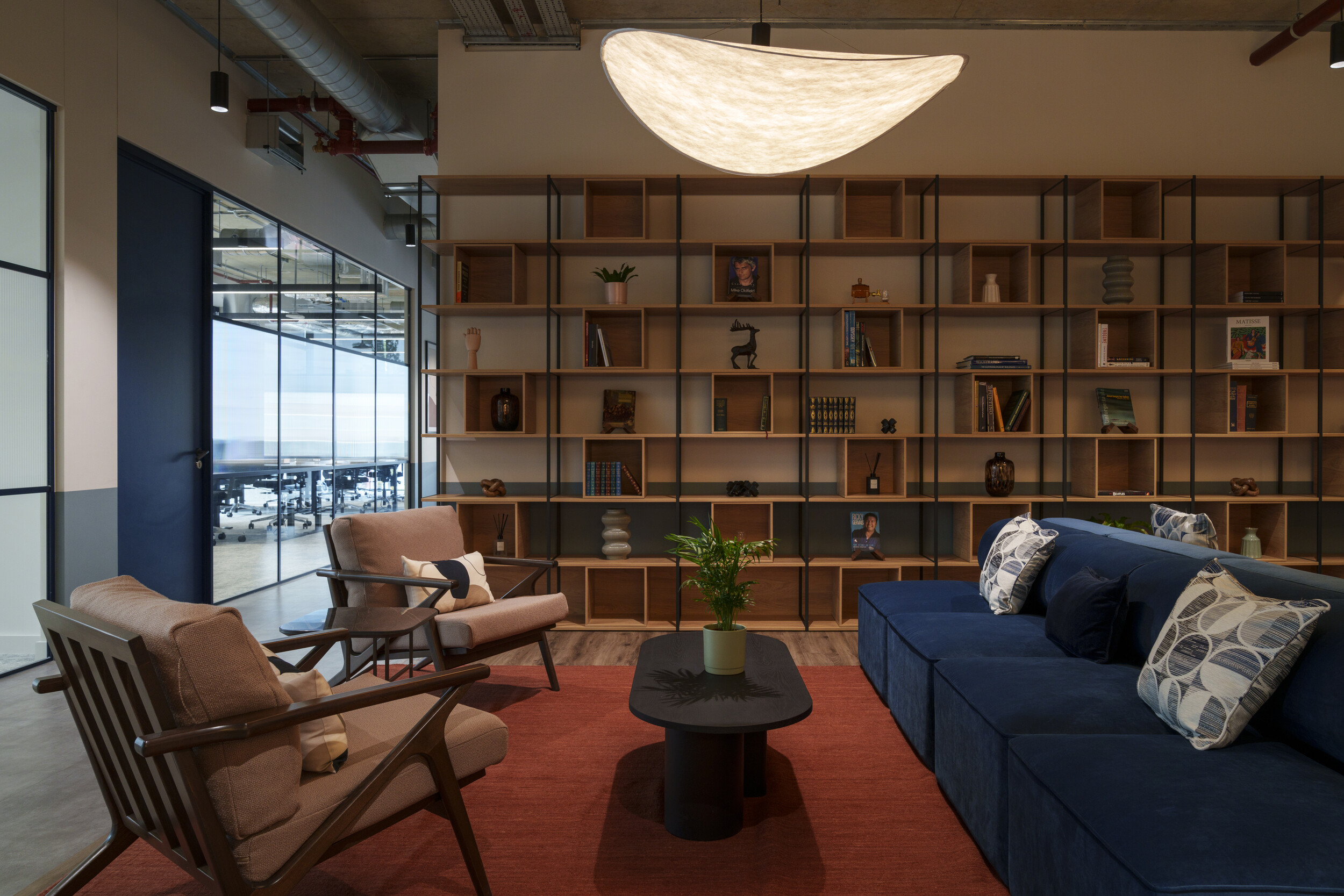 Comfortable lounge seating at Newflex - Reading One Station Hill with a blue sofa, patterned cushions, armchairs, and a large shelving wall beside glazed meeting rooms.