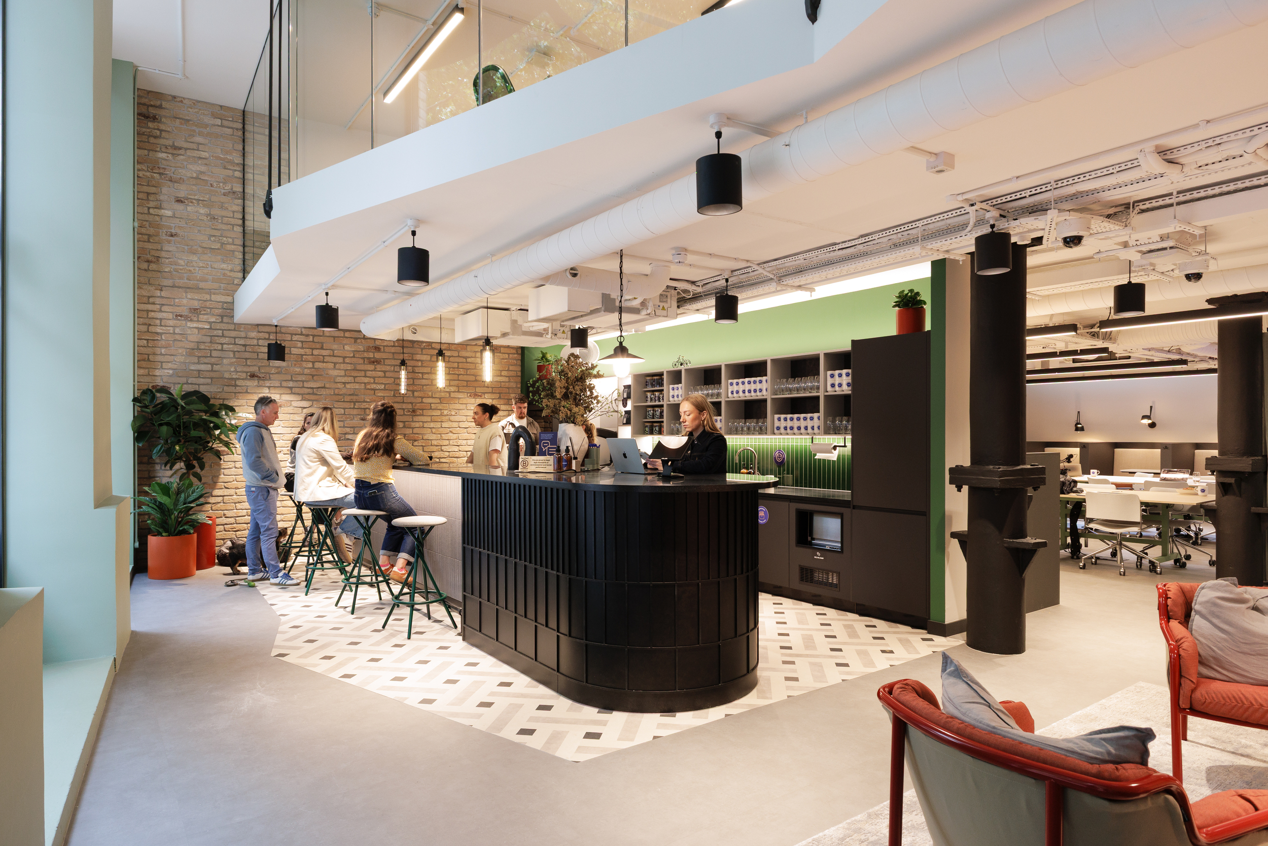 Ground floor café at Work.Life Clerkenwell Green with people socialising around a dark counter and green backdrop, furnished by Platfform.