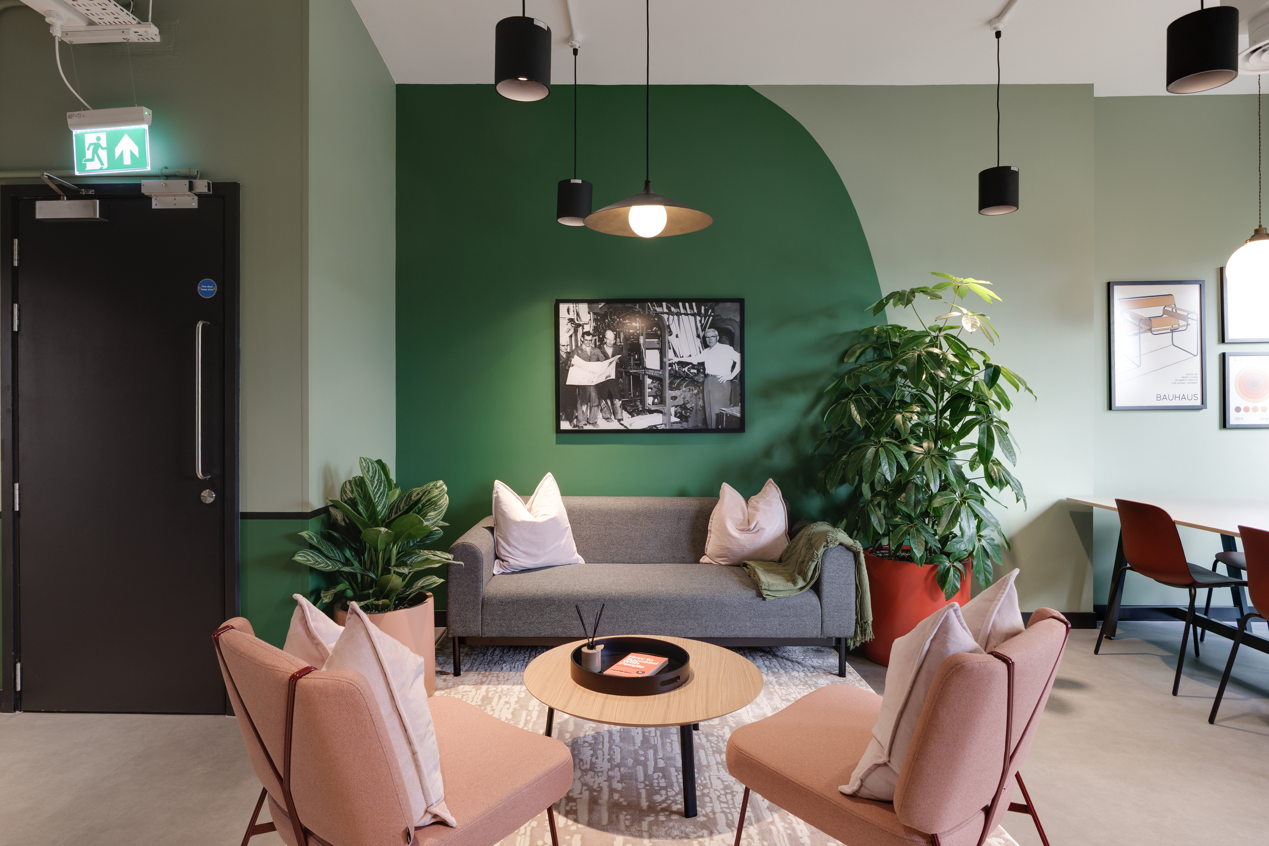 Level 6 lounge area at Work.Life Clerkenwell Green with green walls, soft pink chairs and a grey sofa framed by large indoor plants.